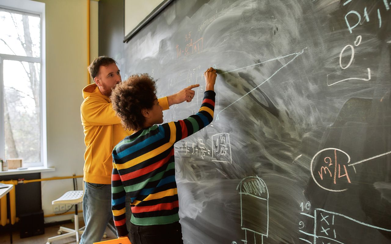 Un enseignant explique au tableau à un élève.